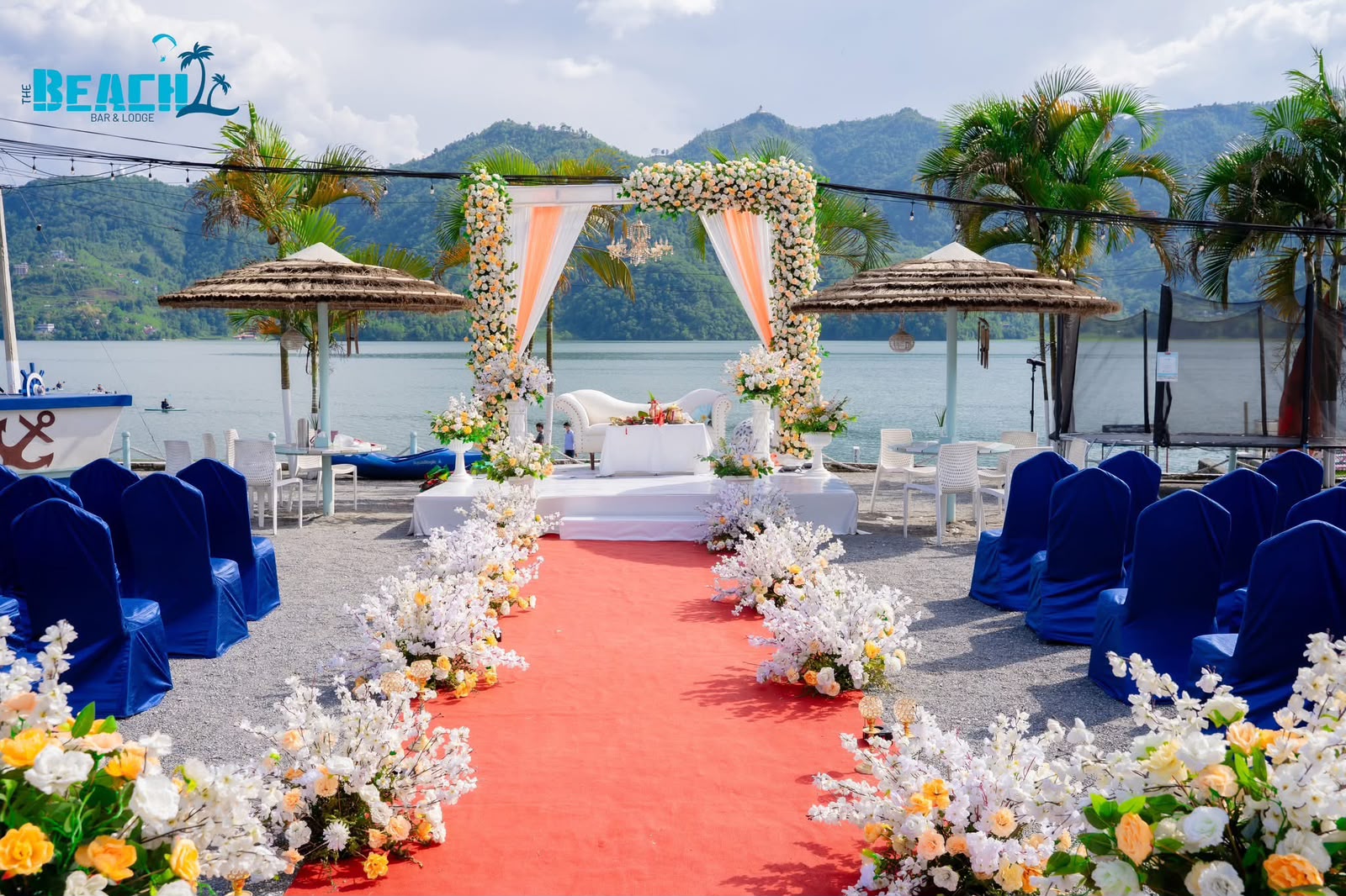Floral arch, blue chairs and a red aisle arranged for a celebration beside Phewa Lake
